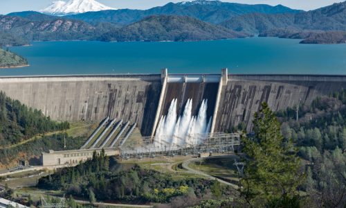 Picture of Shasta Dam surrounded by roads and trees with a lake and mountains on the background A picture of Shasta Dam surrounded by roads and trees with a lake and mountains on the background